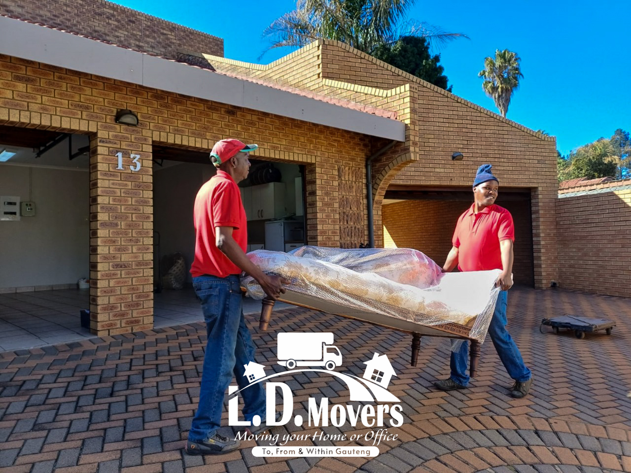 L.D. Movers crew carrying a wrapped sofa out of a house